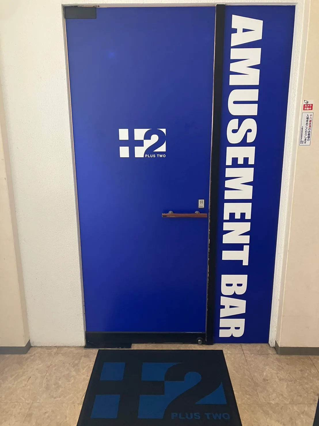 PLUS 2 の入口。青い扉の PLUS TWO ロゴと AMUSEMENT BAR の看板